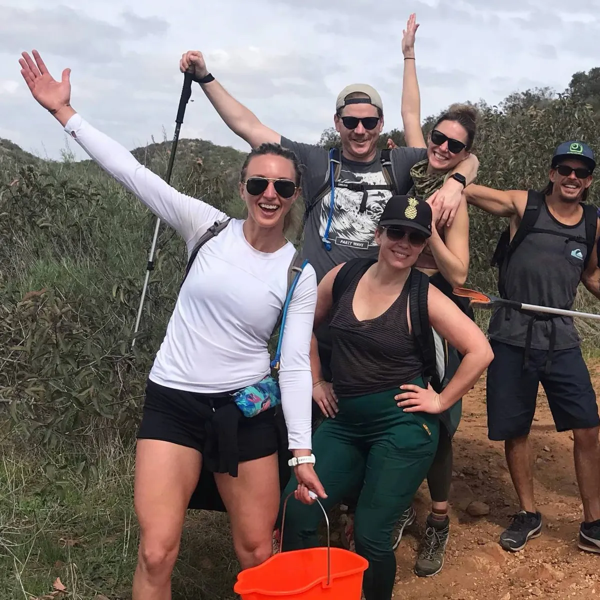 Five volunteers on a trail cleanup, laughing, one holding an orange bucket.